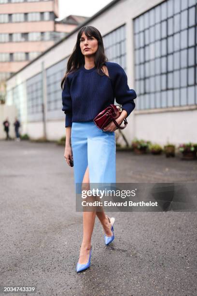 Leia Sfez wears a dark blue ribbed knitted wool pullover with puff sleeves, a burgundy leather bag, a pastel pale slit skirt in leather , pointed...