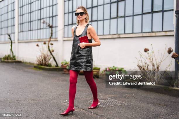 Xenia Adonts wears sunglasses, a black leather monogram logo embossed sleeveless low-neck mini dress from Gucci, burgundy tights, kitten heels...