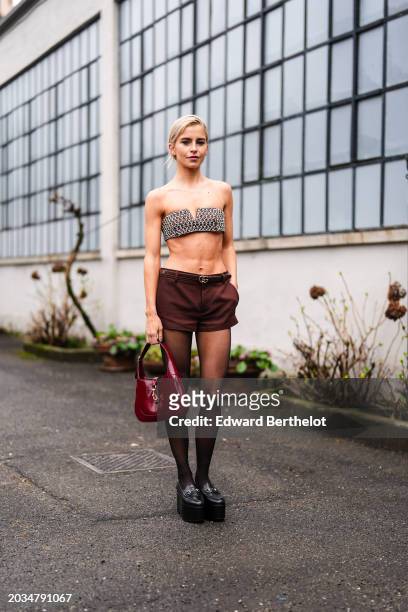 Caroline Daur wears silver mesh bras, a burgundy thin leather belt, mini shorts, a leather bag, black tights, black leather platform shiny shoes,...