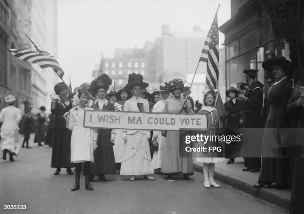 Group of Women's Suffrage activists march in a parade carrying a banner reading 'I Wish Ma Could Vote' circa 1913.