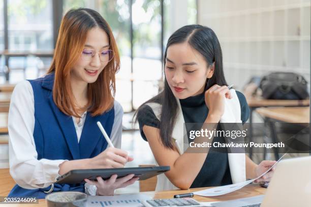 two young gen z women working together on their project using computer tablet and printed charts at a co-working space - z com stock pictures, royalty-free photos & images