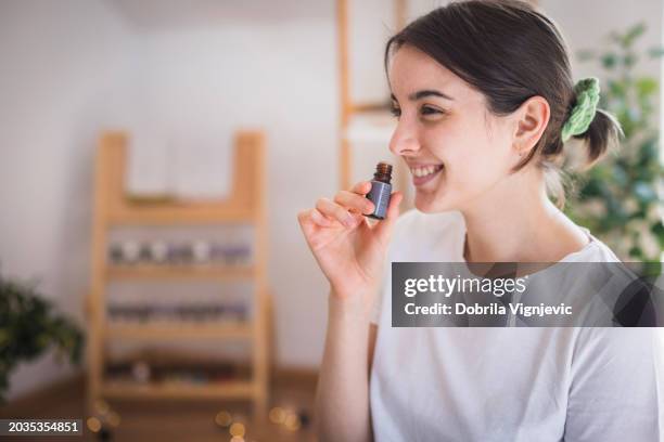 smiling young woman smeling essential oil - aromatherapy stock pictures, royalty-free photos & images