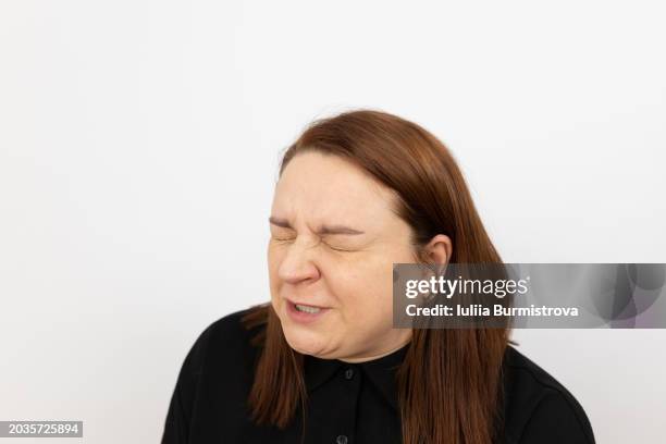 expressive portrait of redhead woman, standing in front of white background with eyes closed and face contorted in grimace - sore eyes stock pictures, royalty-free photos & images