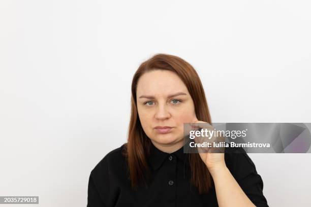 portrait of concerned mature lady pulling skin on cheek, with expression reflecting concern about facial fullness - cheek stock pictures, royalty-free photos & images