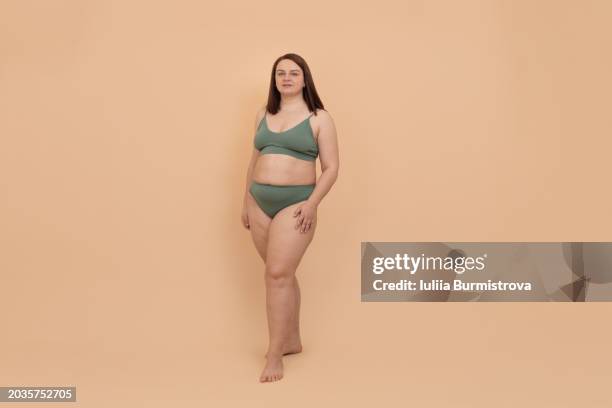 charming obese woman exuding beauty and confidence in bikini, posing in studio against beige background and looking at camera. - exuding stock pictures, royalty-free photos & images