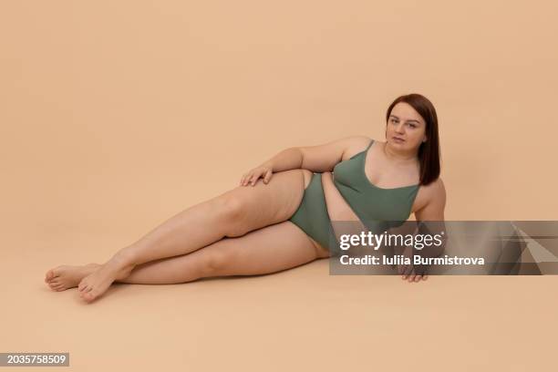 charming obese lady in bikini lying in studio and looking at camera with eyes full of confidence, showing perfection in thick figure. - sous vêtement photos et images de collection