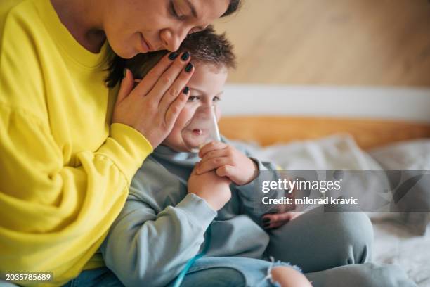 mutter kümmert sich mit einer inhalationsmaske um ihren kranken jungen. - respiratory disease stock-fotos und bilder