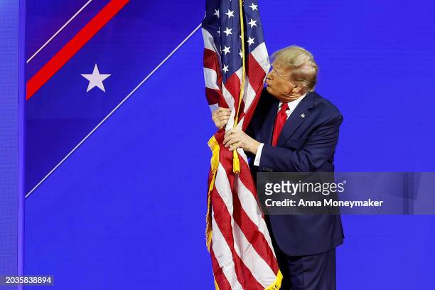Republican presidential candidate and former U.S. President Donald Trump hugs an American flag as he arrives at the Conservative Political Action...
