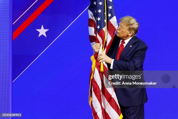 Republican presidential candidate and former U.S. President Donald Trump hugs an American flag as he arrives at the Conservative Political Action...