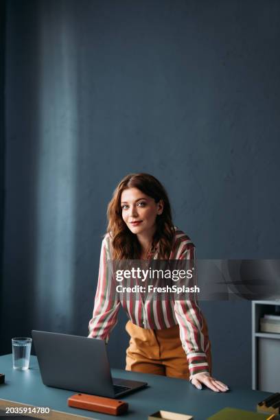 porträt einer berufstätigen frau bei der arbeit in einem stilvollen büro mit einem laptop - vertikal stock-fotos und bilder