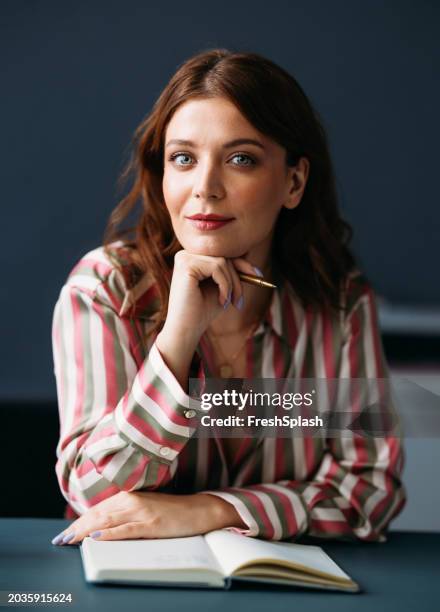 confident businesswoman posing with pen and notebook in office setting - hand on chin stock pictures, royalty-free photos & images
