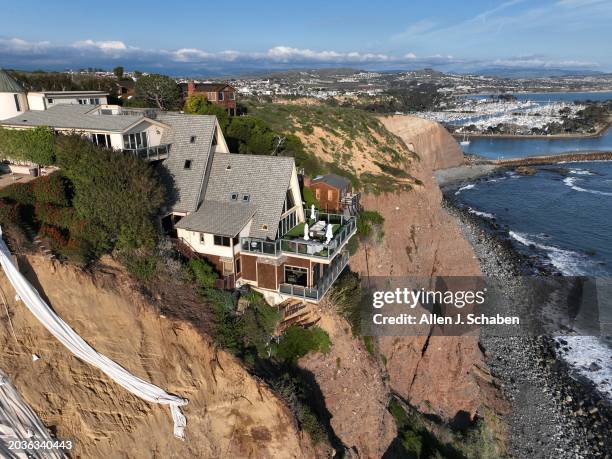 Dana Point, CA An aerial view of a double A-frame cliff-side mansion, between two other mansions affected by a landslide and protective tarps to...