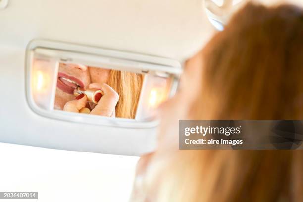 portrait of mature woman sitting in her car applying lipstick using mirror - looking at camera celebrity stock pictures, royalty-free photos & images