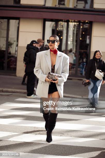 Gili Biegun wears long black boots, a black mini dress, a grey oversized blazer, a red rose or flower neck accessory and a Valentino bag outside...