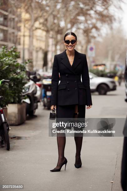 Tamara Kalinic wears a black skirt with a slit, a tailored blazer, a bag, sunglasses, and heels outside Dolce & Gabbana during the Milan Fashion Week...