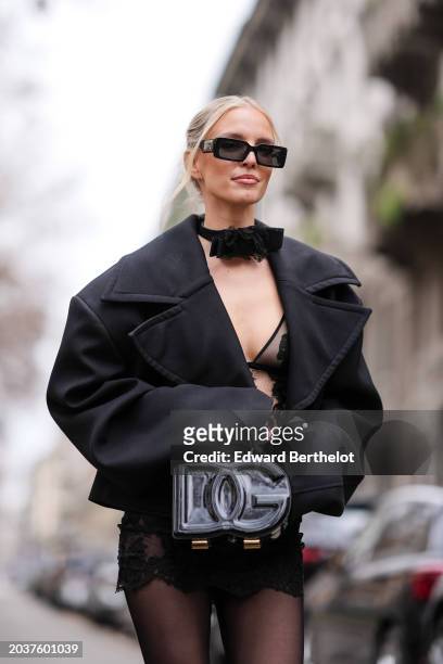 Leonie Hanne wears sunglasses, a bow detail choker, a black oversized blazer jacket , a low-neck black floral embroidery mini dress, a black shiny...