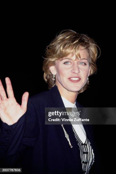 American television host and comedian Ellen DeGeneres, wearing a dark blue blazer over a black macrame waistcoat, over a white crew neck top, attends...