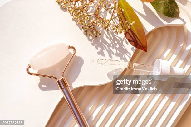 rose quartz facial jade roller, pipette with face serum or massage oil, beauty product ampoule and  branch of a spring plant with pink flowers on a natural concrete background with waves. - ampoule dessin stockfoto's en -beelden