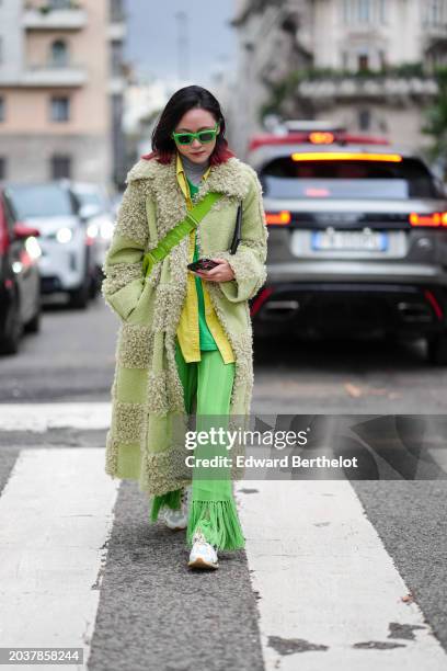Guest wears green sunglasses, a gray turtleneck top, a green long fluffy with checkered / checked patterns, a yellow shirt, green fringed pants,...
