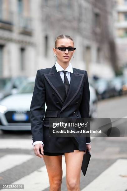 Guest wears sunglasses, earrings, a white shoes , a black tie, a double breasted oversized blazer jacket , a mini skirt, outside Dolce & Gabbana,...