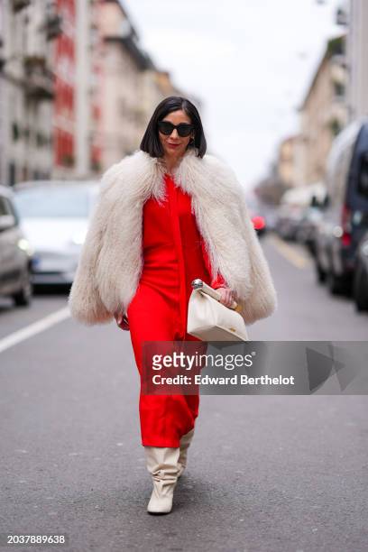 Guest wears sunglasses, a white fluffy oversized jacket , a red dress , white leather gathered boots, outside Dolce & Gabbana, during the Milan...