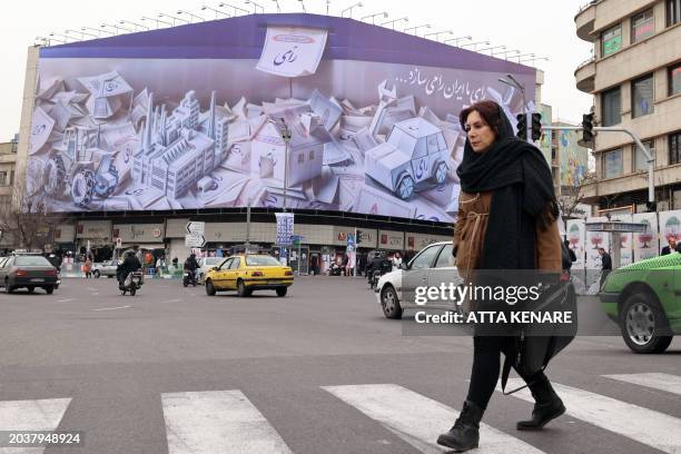 Woman walks in front of a building bearing a giant electoral banner, ahead of the upcoming elections, in Tehran on February 28, 2024. Iran's supreme...