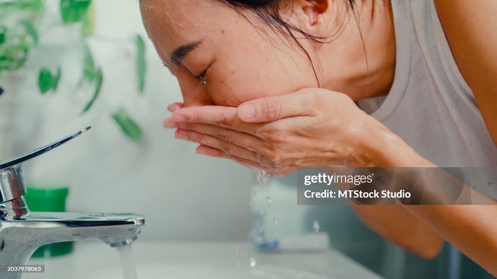 Closeup of young Asian woman having fun facial foam cleaning face in front of mirror in lavatory at home late morning. Routine lifestyle in house.