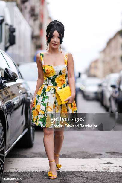 Guest wears earrings, a sleeveless low-neck yellow and green and white floral print pleated mini dress , a yellow leather DG bag, yellow shoes with...