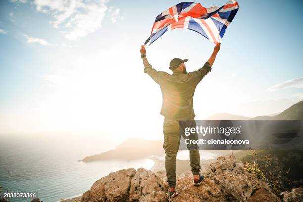 man with the english flag on the background of the sea and mountains - standing banner stock pictures, royalty-free photos & images