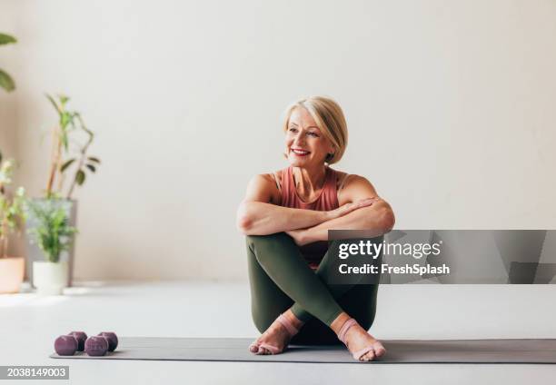 seniorin lächelt während der yogapraxis in einer friedlichen häuslichen umgebung - hell beleuchtet stock-fotos und bilder