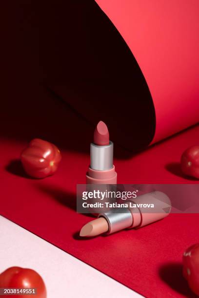 two lipstick tubes with cherry tomatoes on trendy pink and red paper background. luxury commercial photography. front view. - beauty cosmetic luxury studio background stock-fotos und bilder