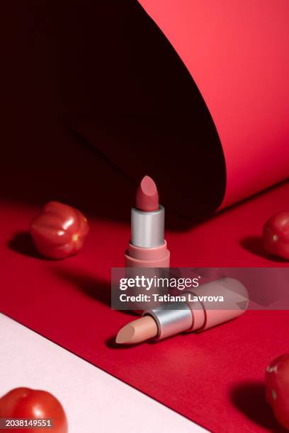 two lipstick tubes with cherry tomatoes on trendy pink and red paper background. luxury commercial photography. front view. - beauty cosmetic luxury studio background photos et images de collection