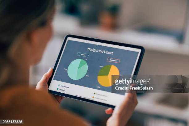 professional woman reviewing financial pie charts on tablet - cost management stockfoto's en -beelden