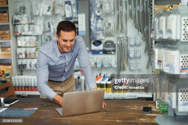 homem bonito jovem usando laptop enquanto trabalha na loja de hardware - só um adulto de idade mediana - fotografias e filmes do acervo