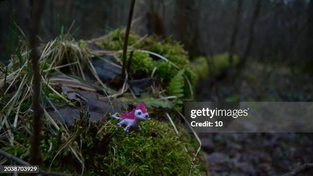 a toy fire frog inspired by bruni from frozen 2, sitting on moss in a forest. the pink toy contrasts with the natural setting. - ship on fire stock pictures, royalty-free photos & images