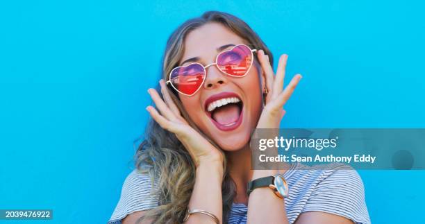 fashion, heart sunglasses and a woman on a blue background while shouting with energy in excitement. summer, smile and beauty with a happy young gen z model in trendy eyewear for style freedom - white heart sunglasses stock pictures, royalty-free photos & images