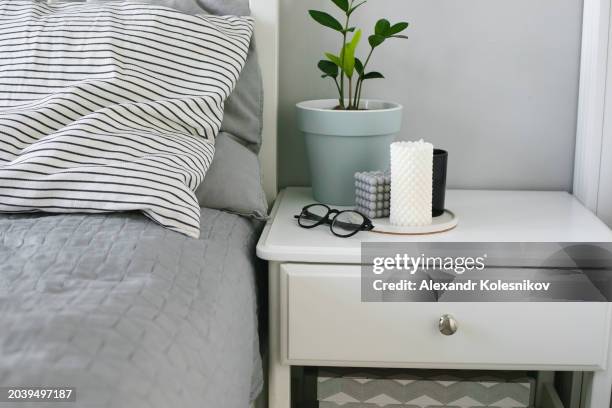 cozy, feminine bedroom with decorative stripe cushions and gray blanket. nightstand with home plant, glasses and candles. - bedside table stock pictures, royalty-free photos & images
