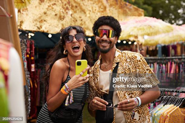 cheerful couple trying sunglasses at market stall - happy sunday stock pictures, royalty-free photos & images