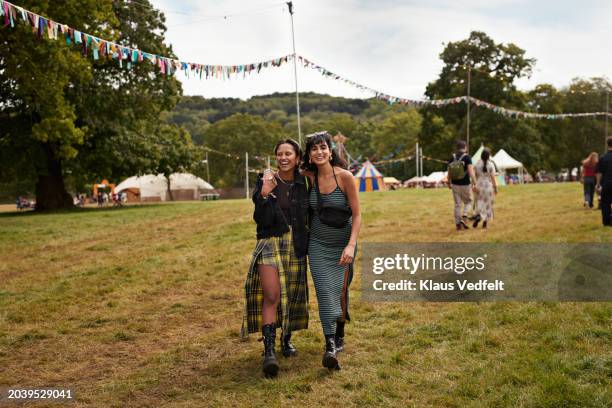 multiracial female friends walking with arms around - music festival grass stock pictures, royalty-free photos & images