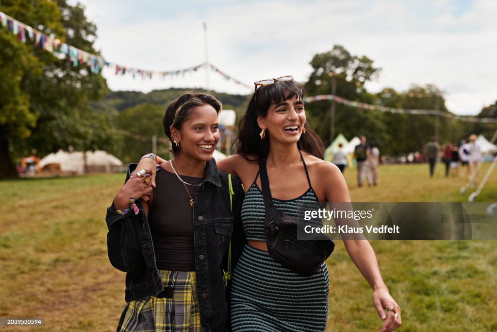 Happy female friends with arms around walking at park
