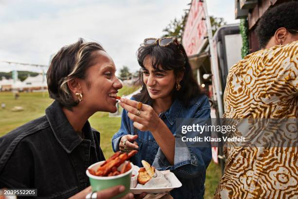 happy woman feeding female friend - streetfood stock-fotos und bilder