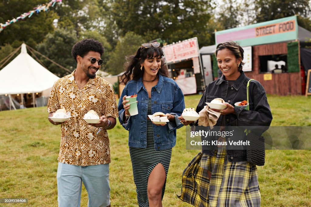 Happy friends carrying street food while walking together