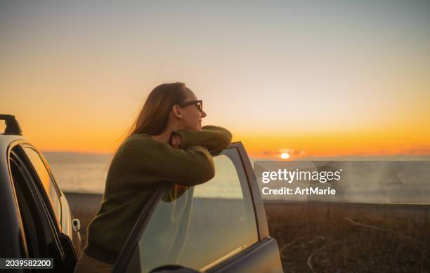 woman enjoying sunset over the sea on the beach near her car. travel, road trip and tourism concept. - horizon stock pictures, royalty-free photos & images