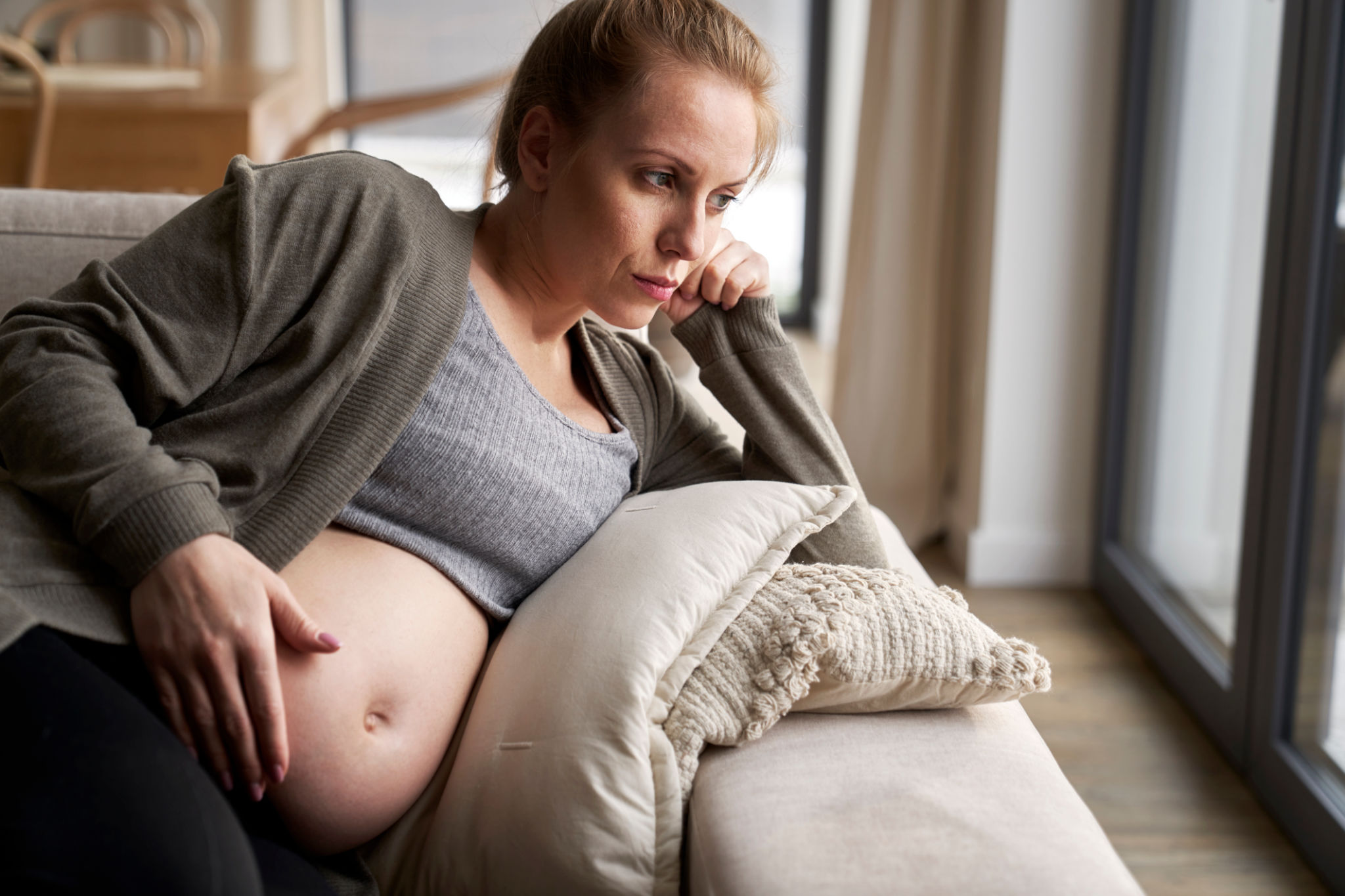 Anxious pregnant woman lying on sofa and touching her abdomen Anxious pregnant woman lying on sofa and touching her abdomen