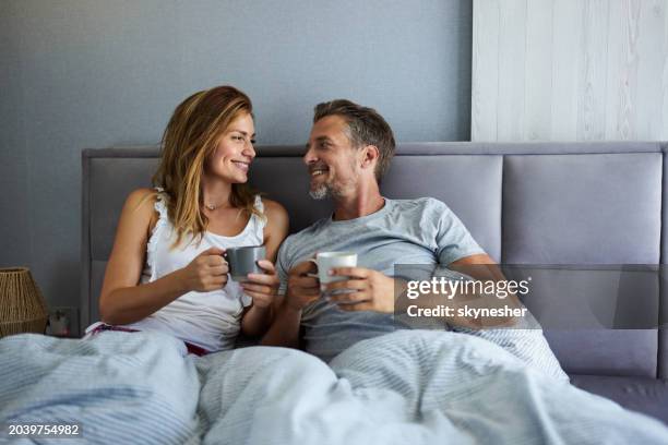 happy couple talking while having coffee during morning in a bed. - ochtend stockfoto's en -beelden