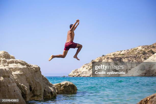 young man jumping into the water from the cliff. - cliff jumping stock pictures, royalty-free photos & images