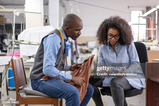young african-american  colleagues in a tailor studio  having discussion, holding a textile product and working on a digital tablet - entrepreneur stockfoto's en -beelden