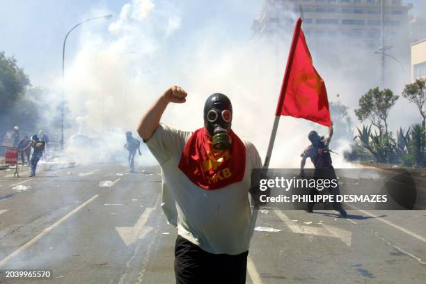 Demonstrator wearing a gas mask and a red flag brandishes his fist during a protest against the G8 summit in Genoa 21 July 2001. Police and...