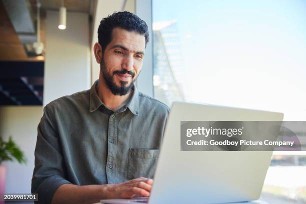 smiling young businessman working on a laptop by an office window - business casual stock pictures, royalty-free photos & images