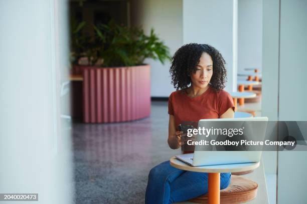 businesswoman working on her phone and laptop in a modern office - partilha de ficheiros imagens e fotografias de stock